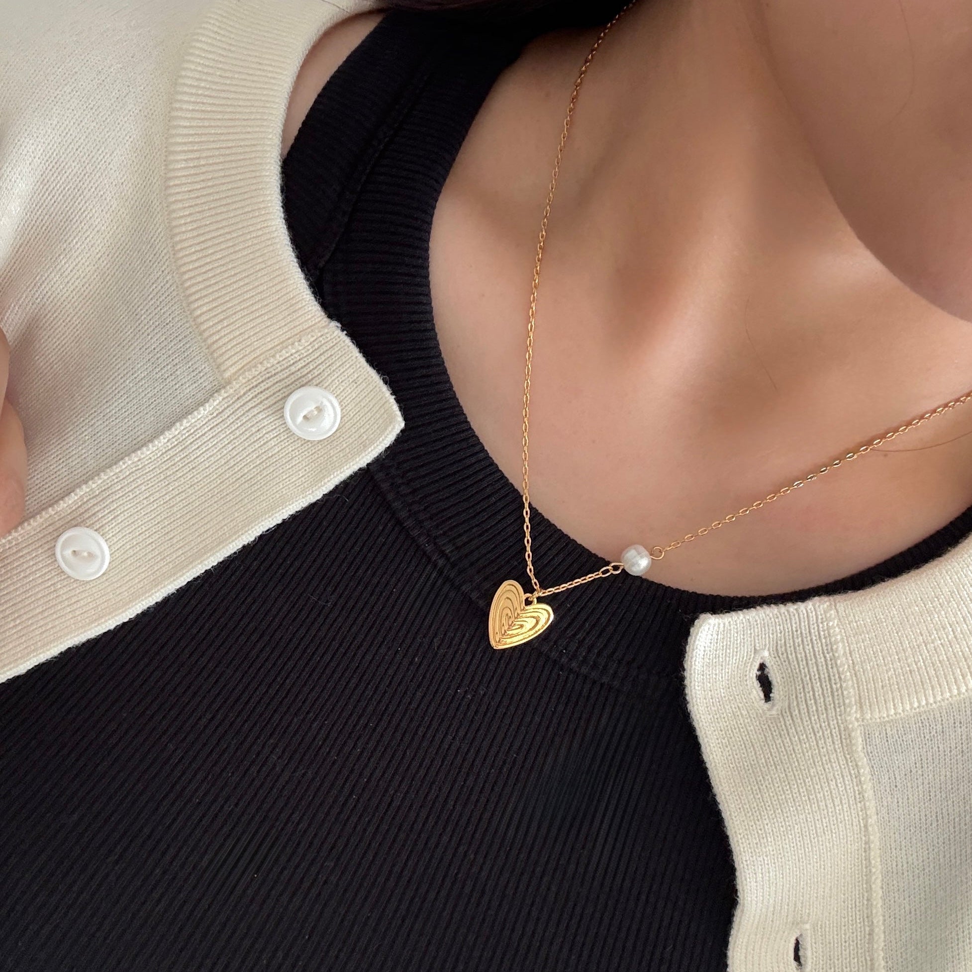 The Veda necklace in 18K yellow gold plating showcased solo, with layered heart design and pearl accent
