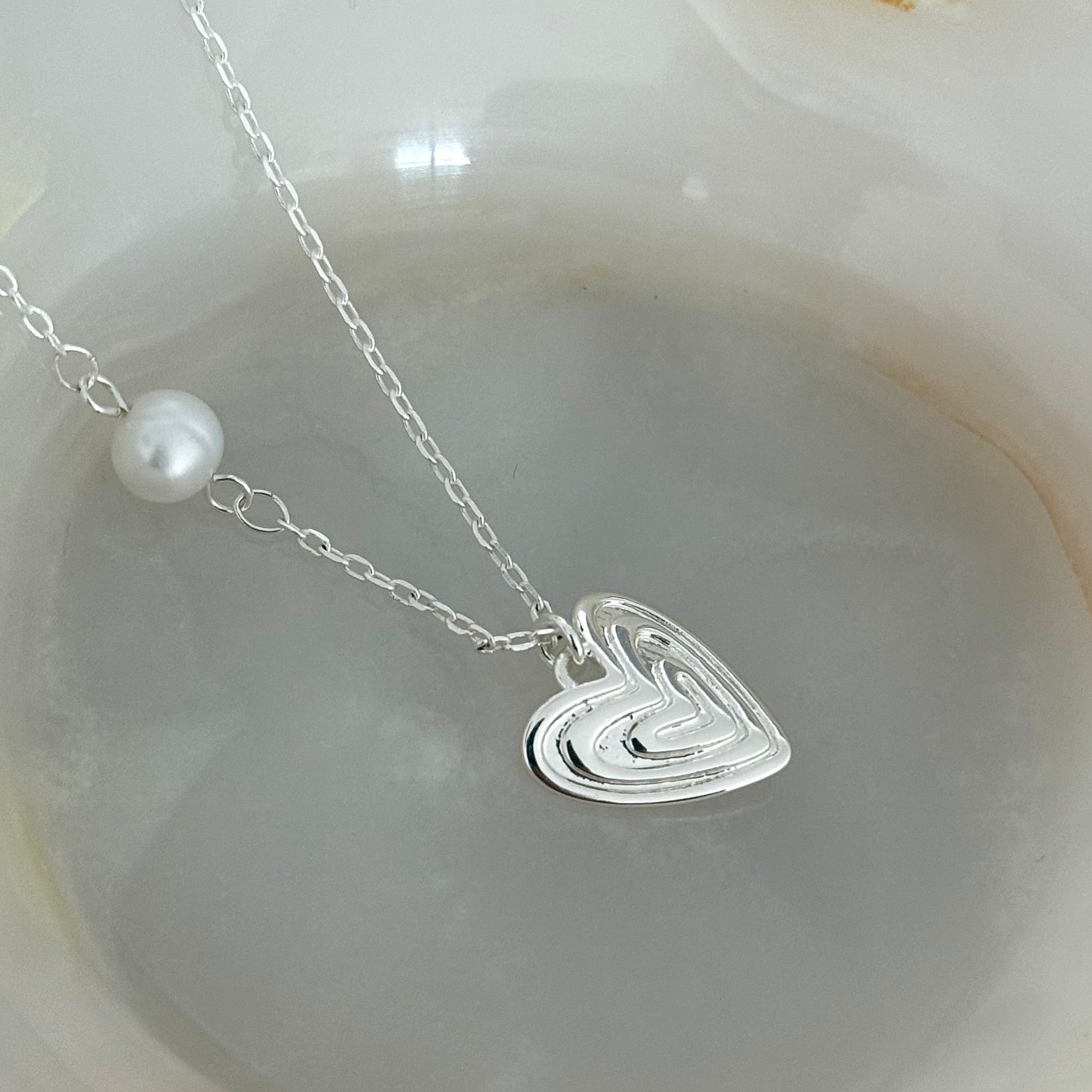 Close-up of the Veda necklace's layered heart pendant in white gold plating, highlighting intricate texture and pearl detail