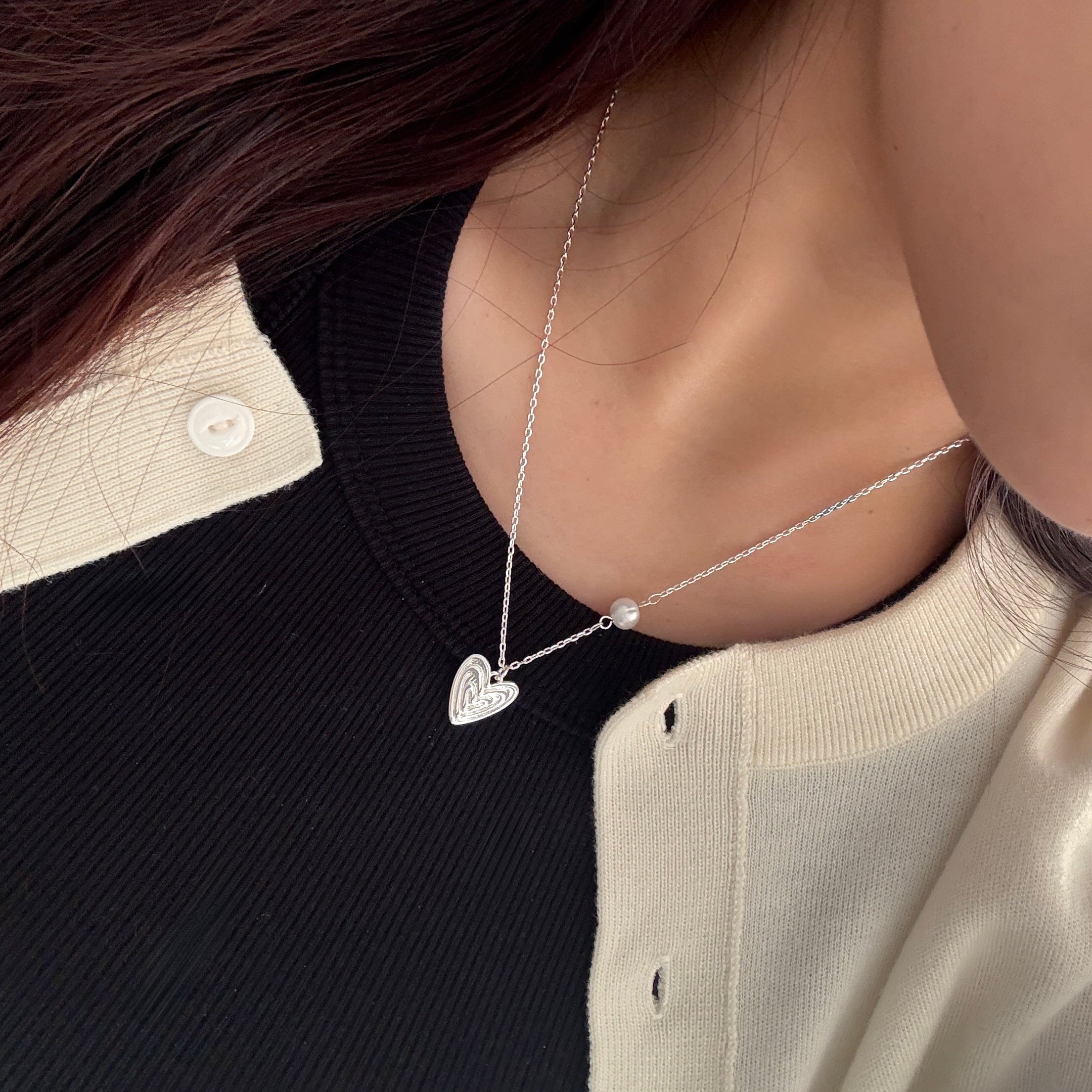 The Veda necklace in 18K white gold plating worn alone, featuring a layered heart pendant and freshwater pearl on delicate chain
